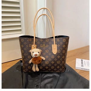 Detail of a brown monogram tote bag with leather handles and a plush bear pendant