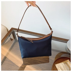 Detail of minimalist dark blue nylon shoulder bag with brown leather handles