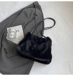 Detail of plush black faux fur shoulder bag with leather straps on a grey blazer