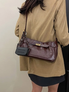 Vintage burgundy shoulder bag with gold twist lock and mini charm on a brown suit