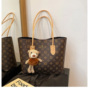 Macro detail of brown monogram tote bag with gold logo and plush bear charm accent