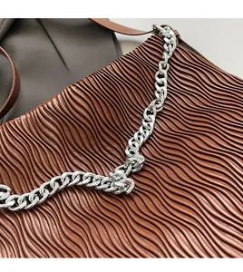 Detailed close-up of brown pleated leather texture and chunky silver metal chain strap