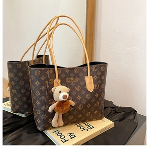 Detail of monogram tote bag with plush bear charm resting on a book with mirror reflection