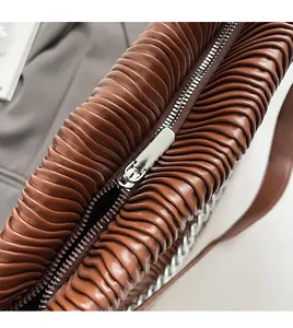 Close-up of smooth metal zipper and textured pleated brown leather on a bucket bag