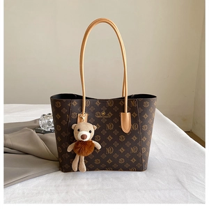 Detail of retro brown tote bag with monogram pattern and cute bear keychain accessory