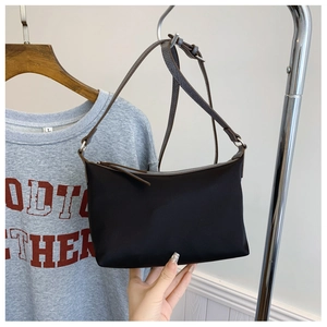 Detail of minimalist black nylon shoulder bag with adjustable dark brown strap and zipper