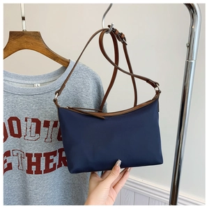 Detail of dark blue nylon shoulder bag with brown leather strap and zipper trim