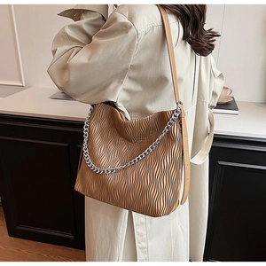Close-up of brown pleated shoulder bag featuring a bold silver chain and leather strap
