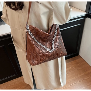 Detail of brown pleated bucket bag with silver chain strap worn with a beige trench coat