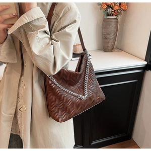 Detail of dark brown pleated hobo bag with silver chain strap on marble tabletop