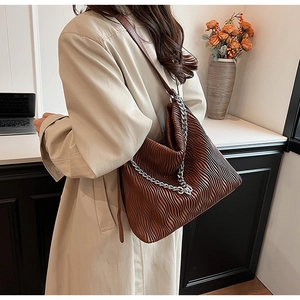 Close-up of brown pleated leather hobo bag with silver chain on model in trench coat