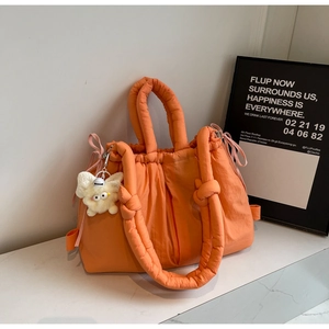Detalle de bolso acolchado naranja con cordón rosa y colgante de peluche blanco suave