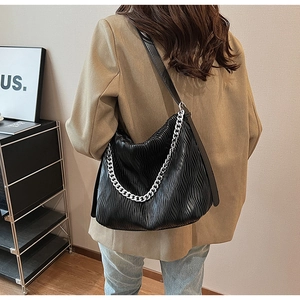 Detail of black pleated faux leather bag with shiny texture and silver chain strap