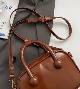 Nahaufnahme der braunen glänzenden Ledertasche auf grauem Sakko mit Schultergurt