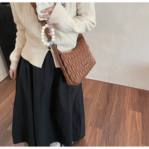 Detail of brown pleated shoulder bag with decorative white beads on model