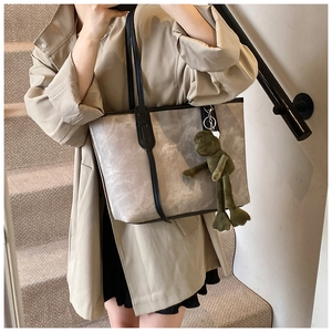 Detail of grey suede tote bag with black leather straps and green frog plush charm accessory