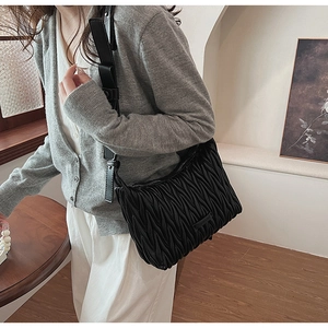 Detailed close-up of a black pleated matelassé shoulder bag worn by a model in a room
