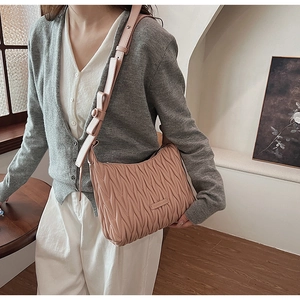 Close-up of pink matelasse shoulder bag with wide strap worn by a model in interior setting