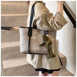 Macro view of textured grey tote bag with green plush frog pendant detail and black straps