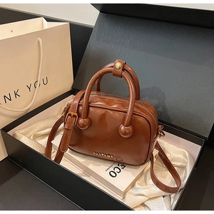 Detailaufnahme einer braunen glänzenden Boston-Tasche mit Goldbeschlägen im Geschenkkarton