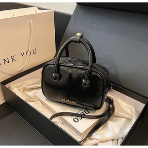 Detail einer schwarzen Lackleder-Bostontasche mit goldenem Logo in edler Geschenkbox