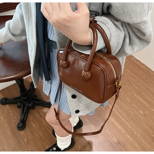 Detailaufnahme der dunkelbraunen Lacklederhandtasche mit goldenem Logo und Riemen