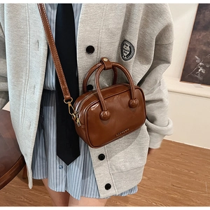 Detail einer dunkelbraunen Vintage-Handtasche mit Goldlogo und rundem Tragegriff
