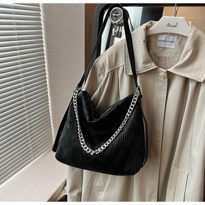 Detail of black pleated shoulder bag with silver chain strap on khaki trench coat