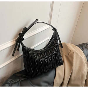 Detailed view of black ruched shoulder bag featuring bow detail and pleated leather texture