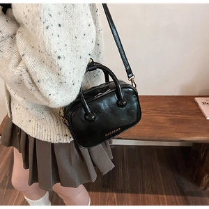 Detail einer schwarzen Handtasche aus glänzendem Kunstleder mit goldenen Beschlägen