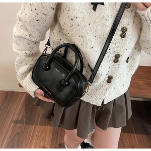 Detail der schwarzen glänzenden Handtasche mit goldenem Logo am Model in stilvoller Umgebung
