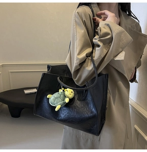 Dettaglio della borsa tote in pelle nera con un simpatico ciondolo a tartaruga verde