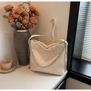 Detailed close-up of cream pleated bucket bag with silver chain and textured leather finish