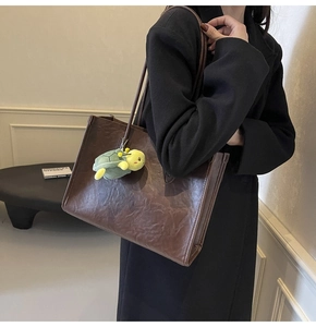Dettaglio della borsa tote in pelle marrone scuro con trama vintage e ciondolo a tartaruga