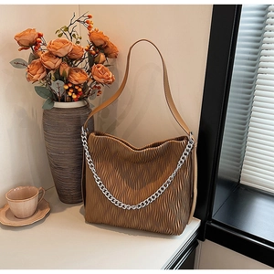 Brown pleated bucket bag with silver metal chain strap in a warm elegant home setting