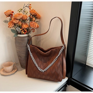 Detail of a brown pleated shoulder bag with silver chain and vertical wave texture