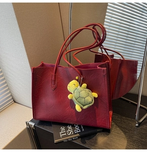 Dettaglio della borsa tote rosso scuro con grana pelle e ciondolo a tartaruga verde