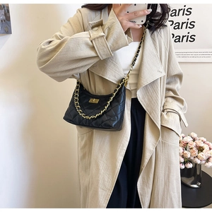 Dettaglio borsa trapuntata nera con catena dorata indossata su un trench beige elegante