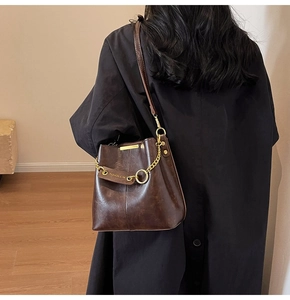 Detail of dark brown leather bucket bag with gold chain and fashion pendant on model