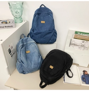 Three denim backpacks in navy, light blue, and black with leather logo and front pocket