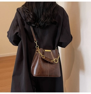 Detail of vintage dark brown bucket bag with oil-wax leather texture and gold chain link