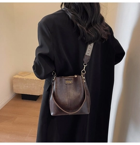 Détail du sac seau marron foncé avec logo doré et bandoulière tissée à motifs