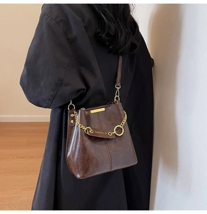 Detail of retro dark brown bucket bag showing oil-wax leather texture and gold chain link
