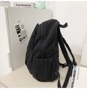 Detail of black denim backpack side pocket and durable padded straps in minimalist style