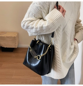 Detail of vintage black leather bucket bag with gold chain strap on a white sweater