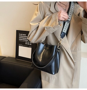 Detail of black glossy bucket bag with patterned webbing strap and gold hardware accents