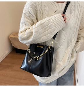 Detail of black glossy bucket bag featuring a bold gold chain and fashion leather tag