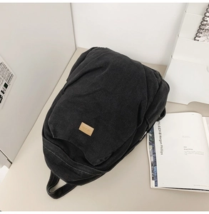 Detail of washed black denim backpack with a brown leather logo patch on surface
