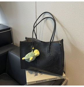 Dettaglio di borsa tote in pelle nera con un piccolo portachiavi a forma di tartaruga