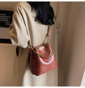 Detail view of brown leather bucket bag with gold chain strap on beige trench coat outfit